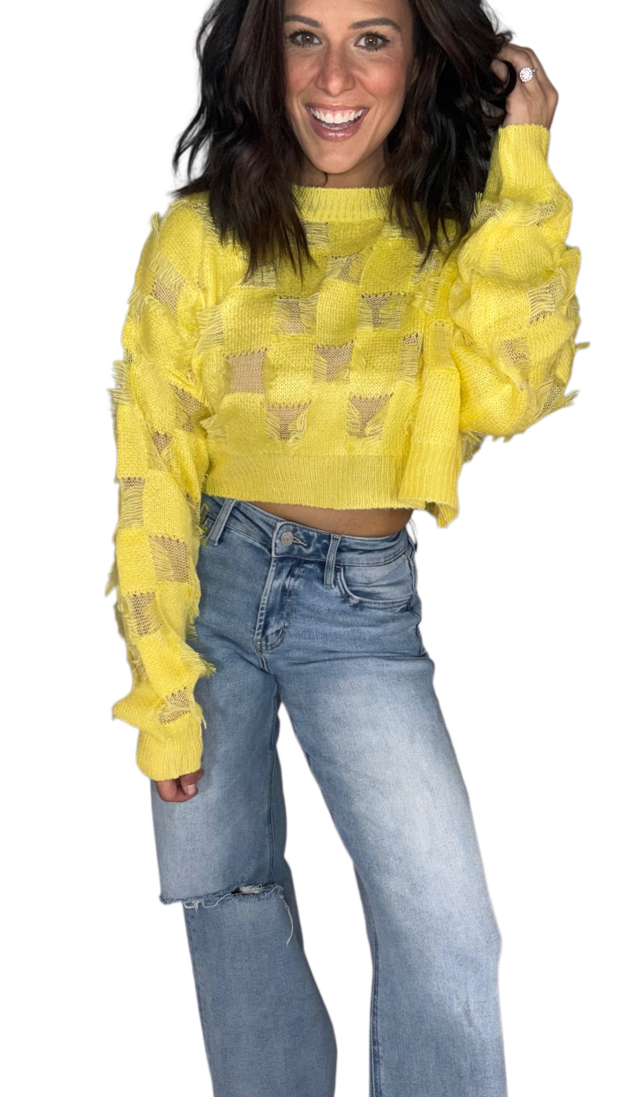 Woman wearing a yellow relaxed fit sweater top with distressed details, paired with medium washed jeans on a white background