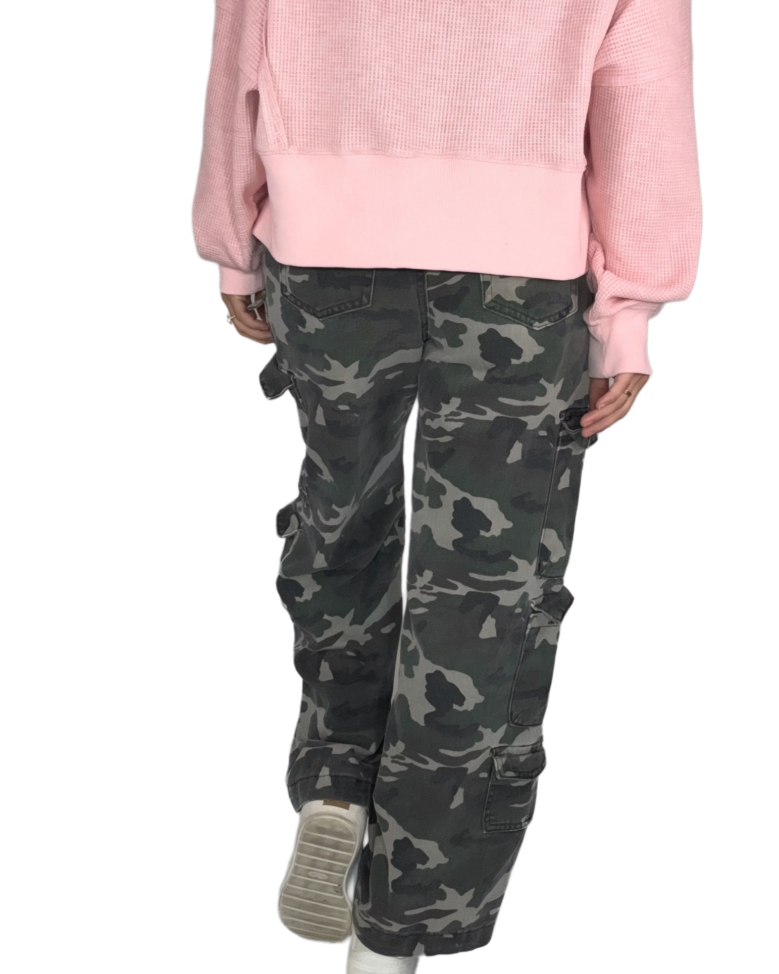 Back profile of a woman wearing a pink sweater and camouflage pants on a white background