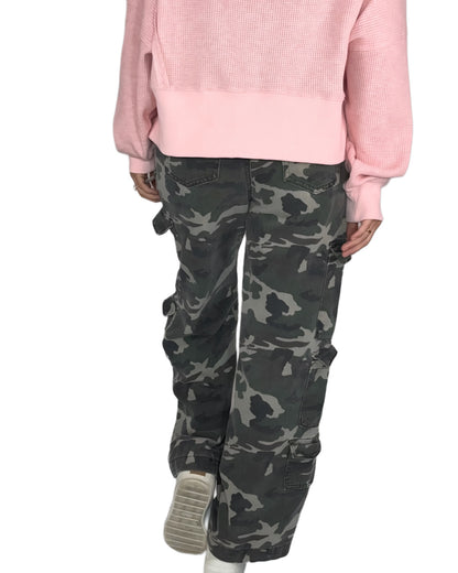 Back profile of a woman wearing a pink sweater and camouflage pants on a white background