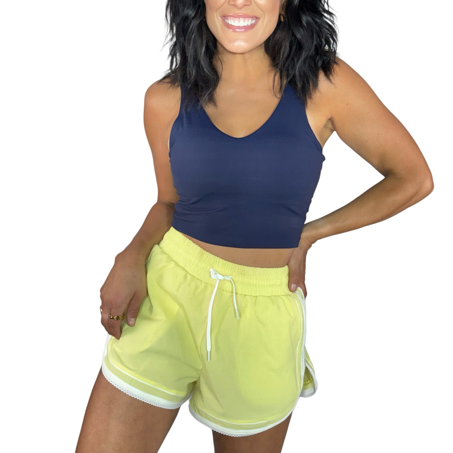 Woman wearing a navy active tank with pale yellow active shorts with lace trim on a white background