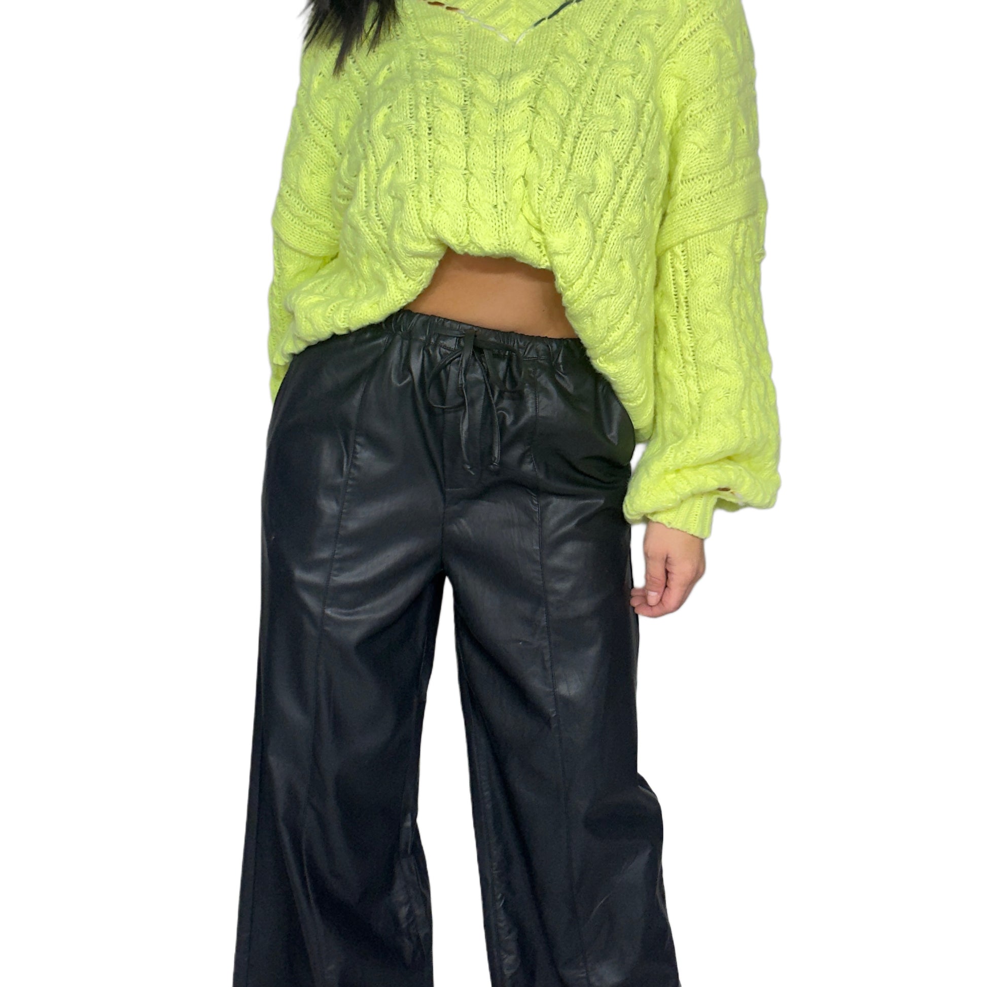 Close up of a woman wearing a bright yellow sweater and black leather pants on a white background
