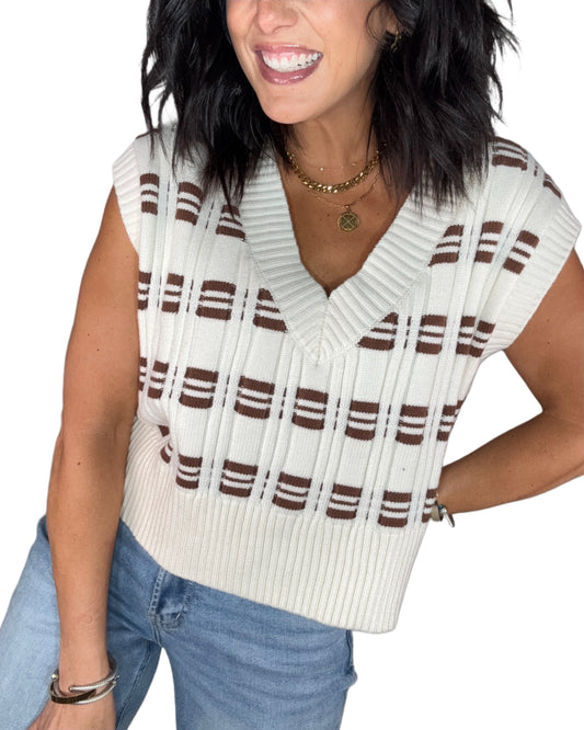 Woman wearing a white and brown striped sweater vest with blue jeans on a white background