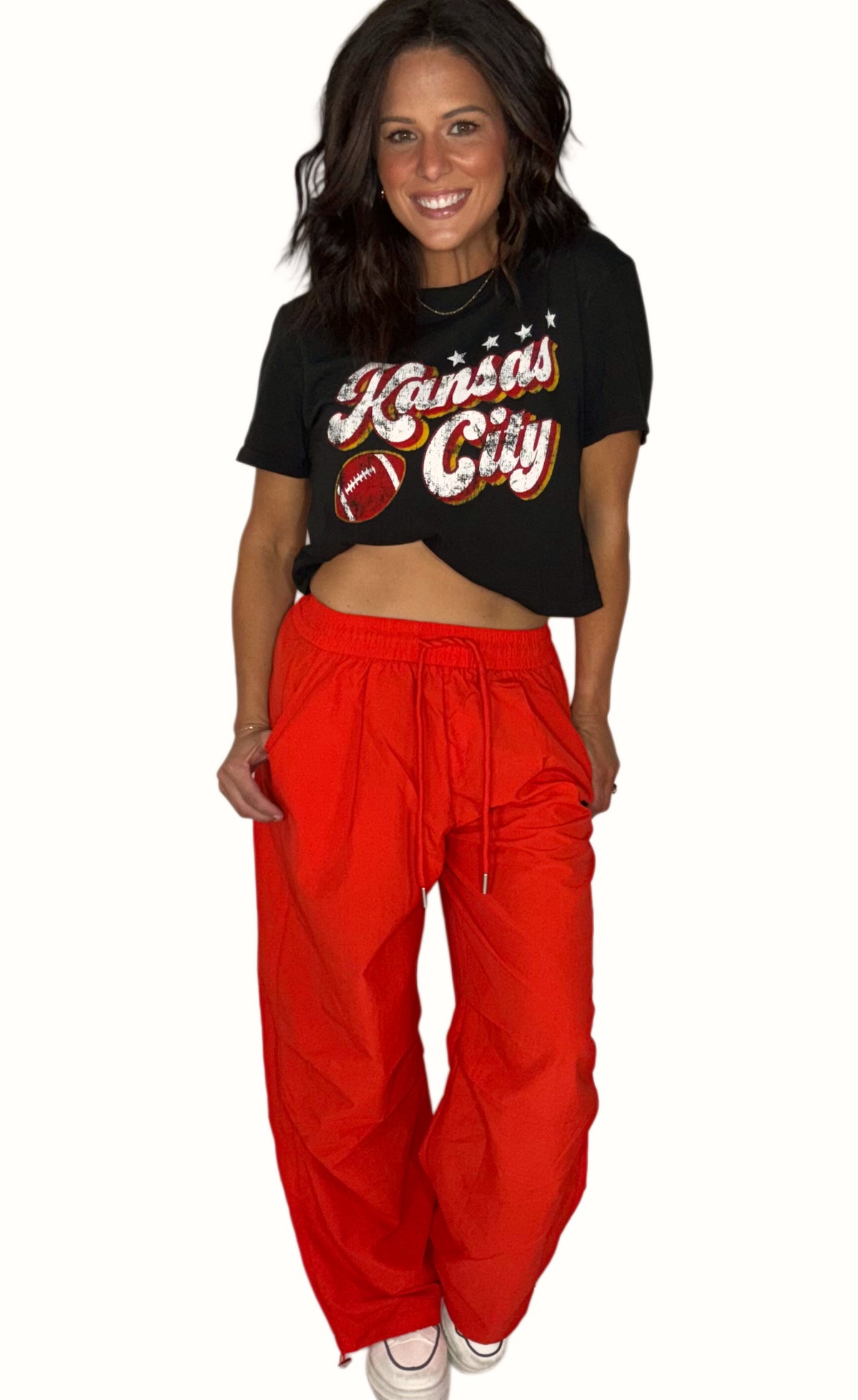 A woman modeling a black cropped graphic t-shirt with 'Kansas City' in white and red lettering, paired with bright red drawstring pants, against a plain white background.
