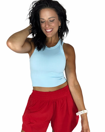 Woman wearing red active shorts with a ribbed sky blue tank top on a white background