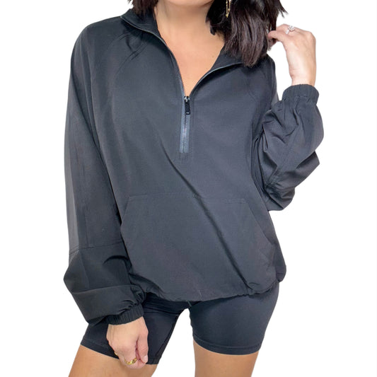Woman wearing black quarter zip active jacket, black shorts and a white background