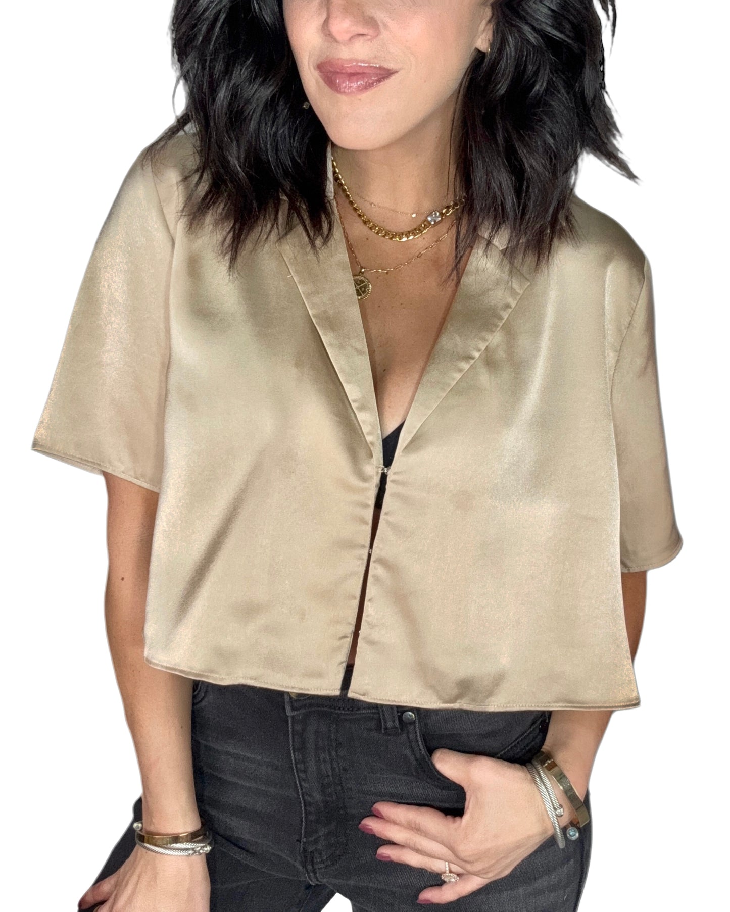 Close up of a woman wearing a gold satin blouse and dark jeans on a white background