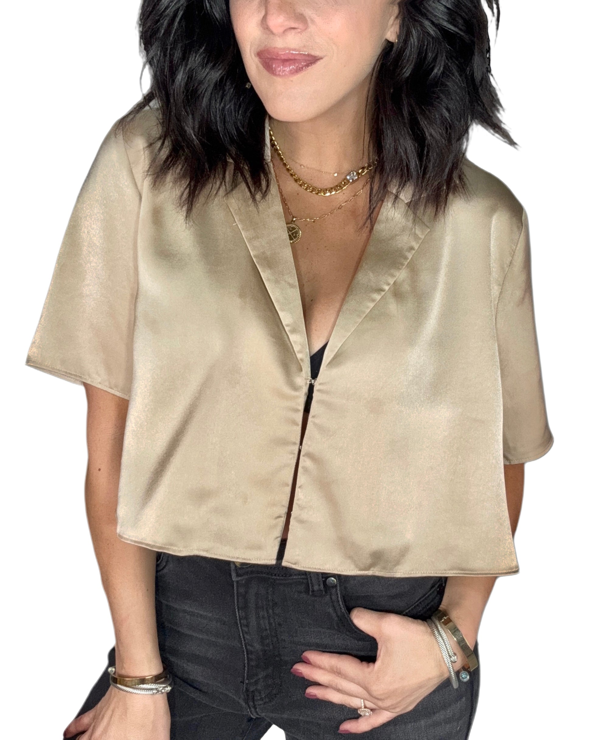 Close up of a woman wearing a gold satin blouse and dark jeans on a white background
