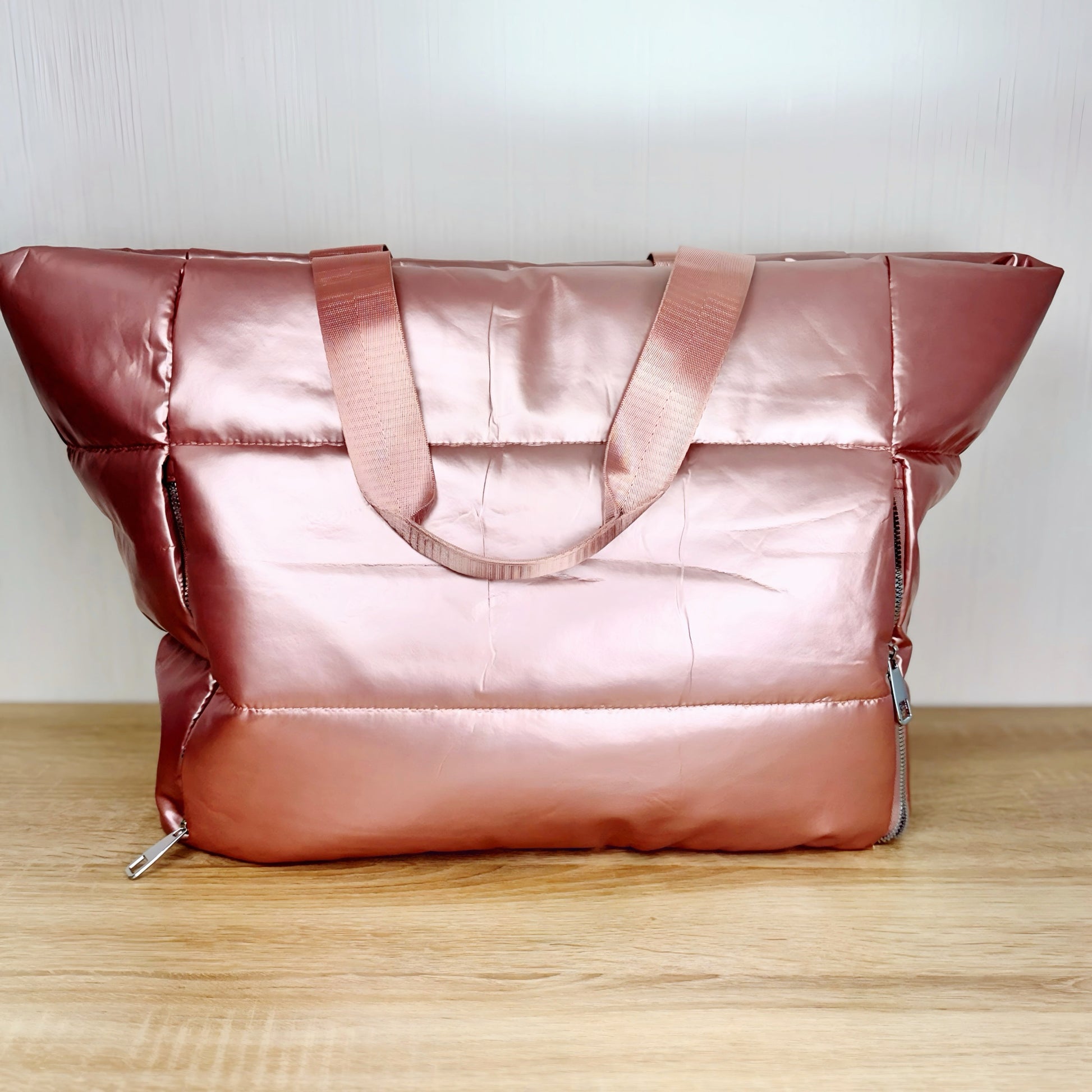 large pink puffer travel tote bag on a light wood table and white background
