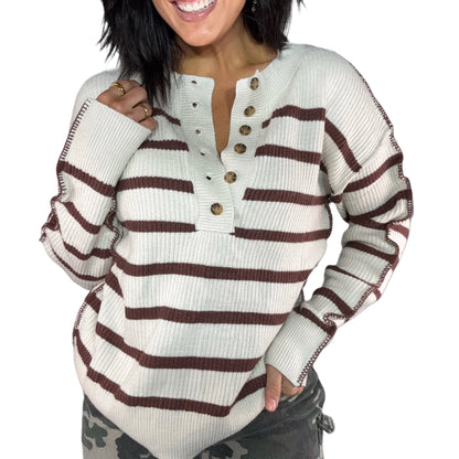 Close up of a woman wearing a white sweater with brown stripes on a white background