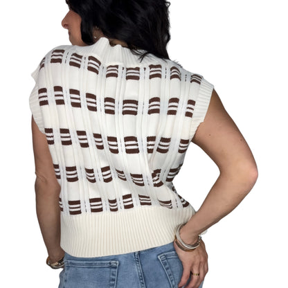 Back profile of a woman wearing a white and brown striped sweater vest with blue jeans on a white background