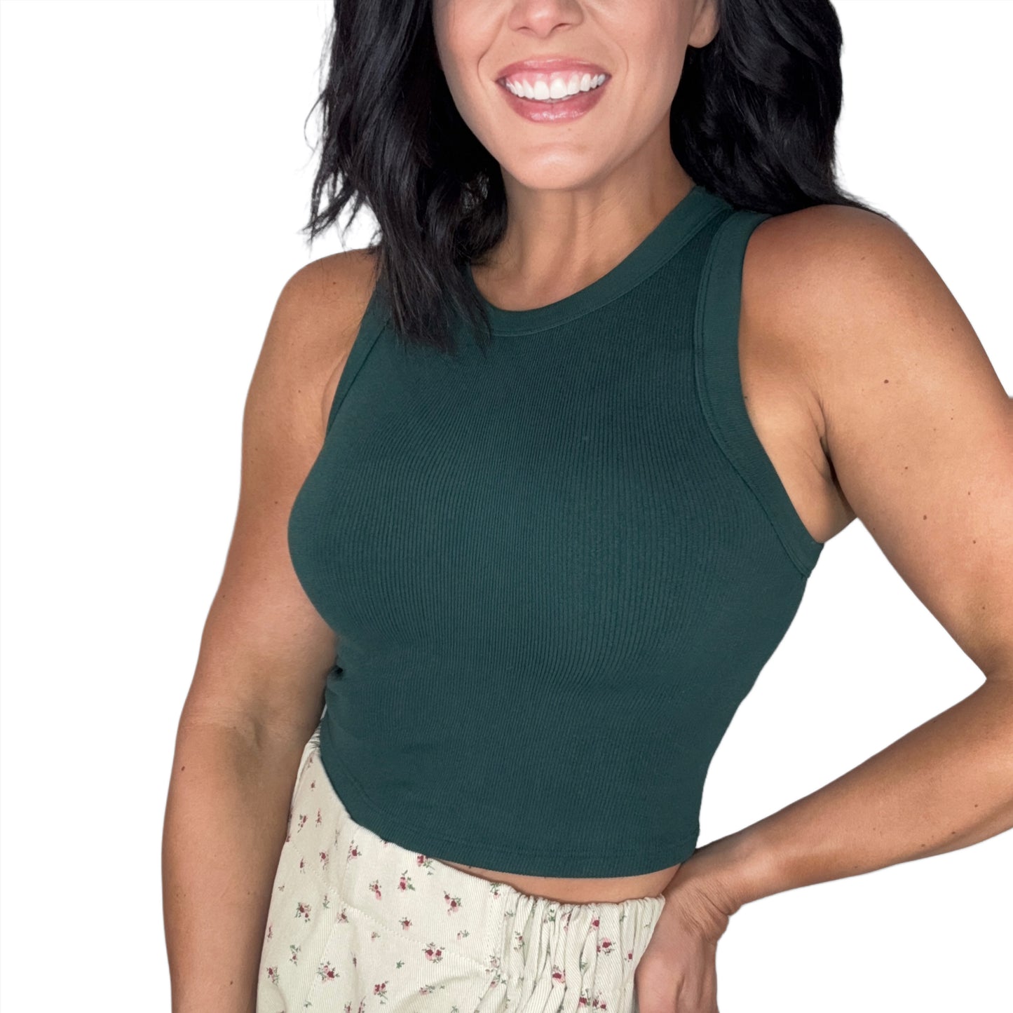 Side profile of a woman wearing a green ribbed tank top, floral shorts, on a white back ground