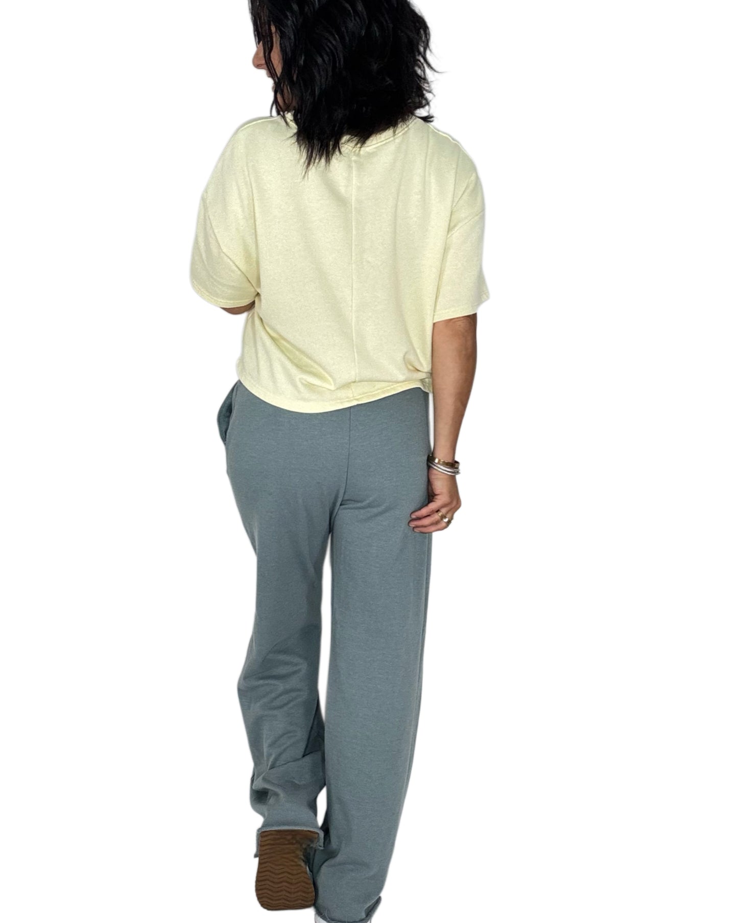 Back profile of a woman wearing blue grey sweat pants with a yellow tee on a white background
