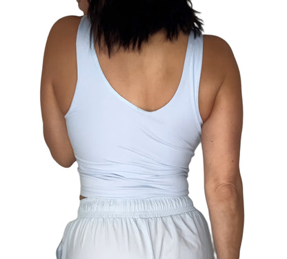 Back profile of a woman wearing a light blue sleeveless active tank and matching pants on a white background