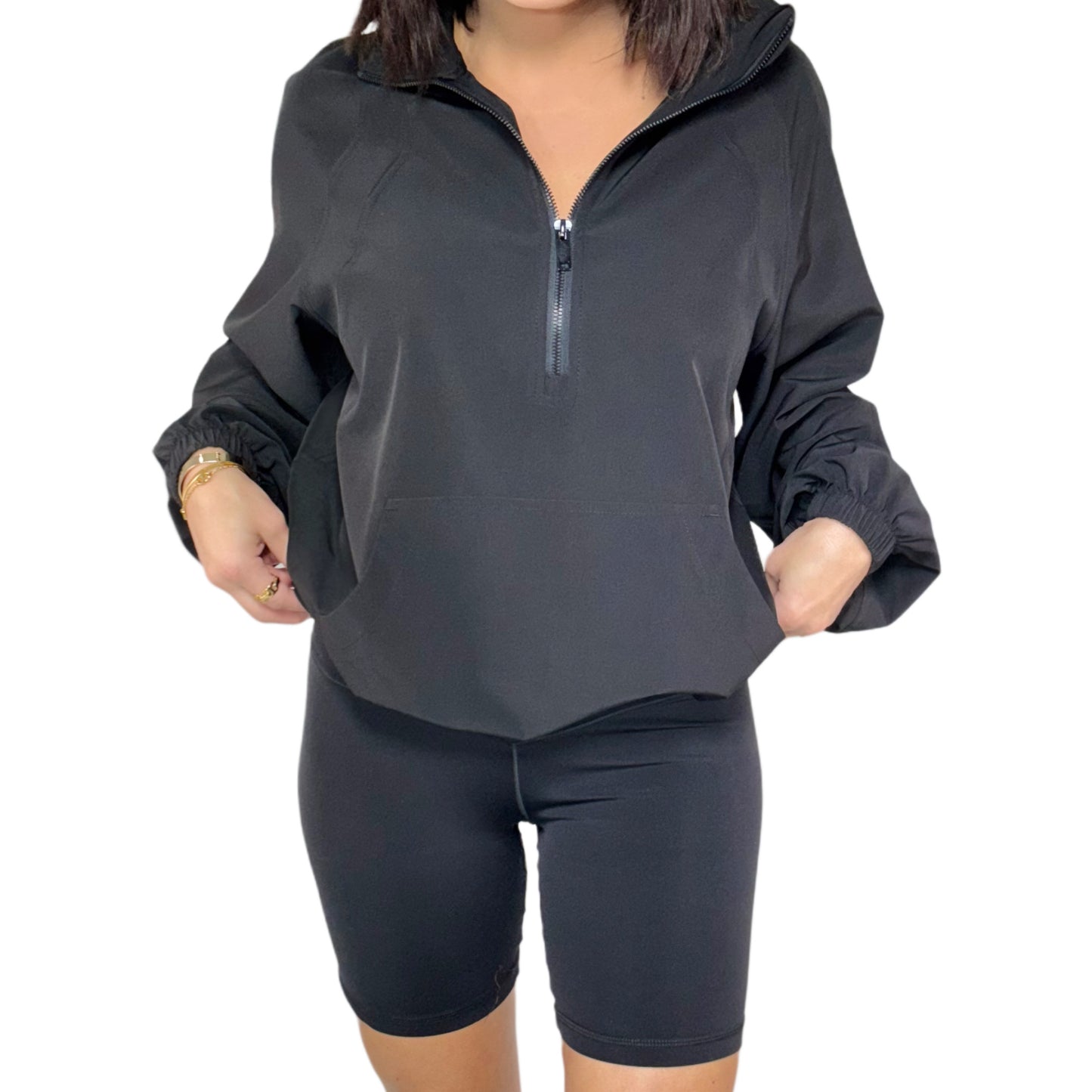 Person wearing a black athletic outfit with a quarter-zip top and shorts on a white background