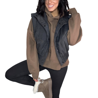 Woman wearing a black vest over a brown oversized hoodie on a white background