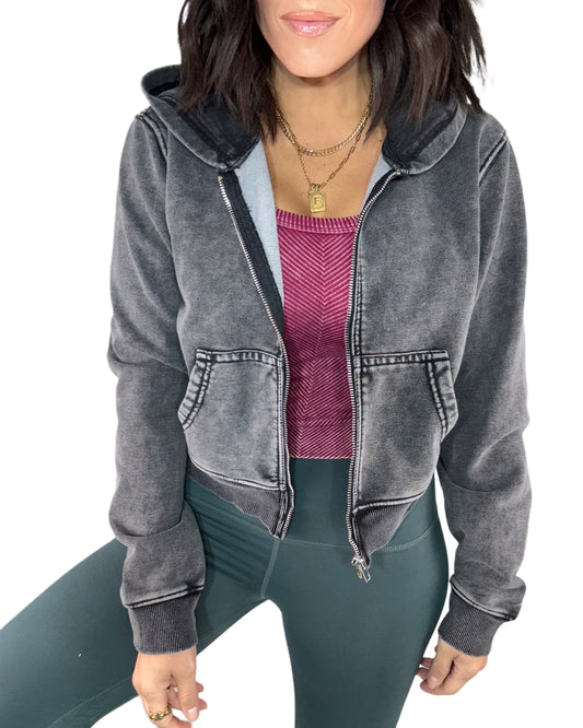 Woman wearing a acid washed gray hoodie over a red top and green leggings on a white background