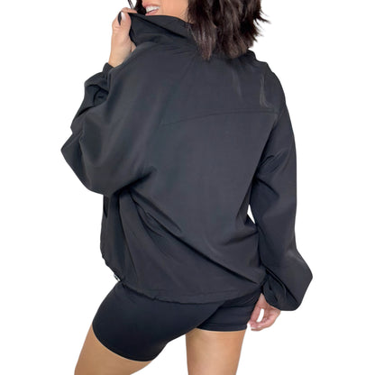 Woman turned around wearing a black quarter zip jacket and shorts on a white background