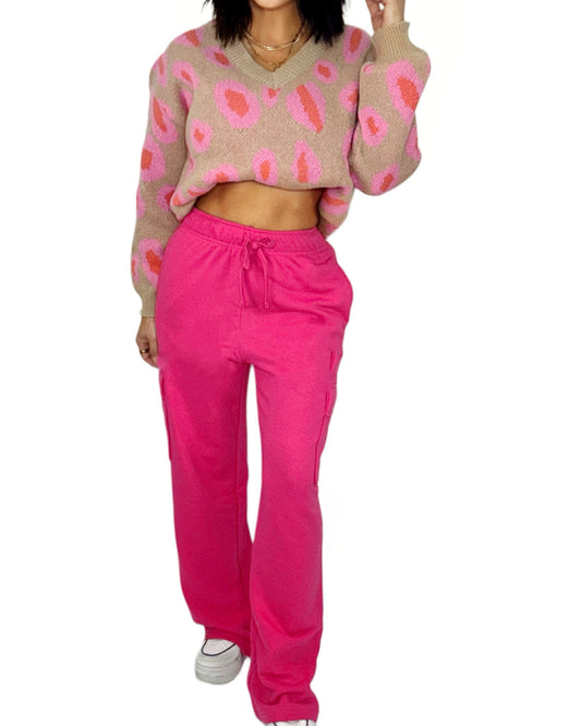 Woman wearing a patterned sweater and bright pink pants on a white background