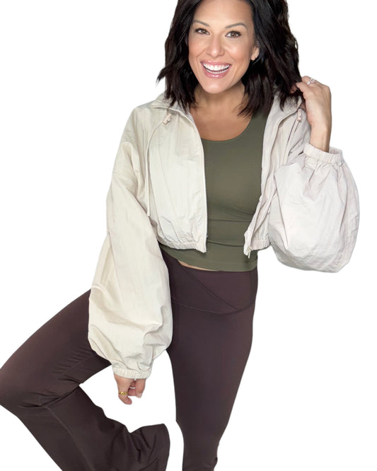 Woman wearing a beige jacket, green top, and brown pants on a white background