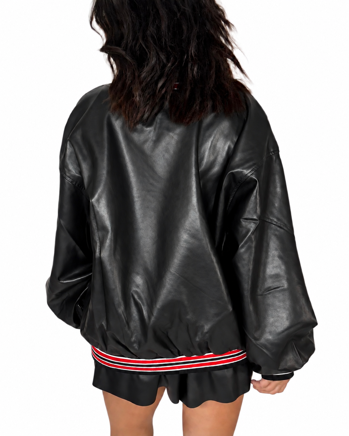 Back profile of a woman modeling a black faux-leather varsity jacket with red and white striped ribbed collar, cuffs, and hem, paired with black shorts against a plain white background.