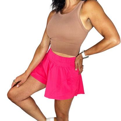 Person wearing a beige tank top and pink skirt on a white background
