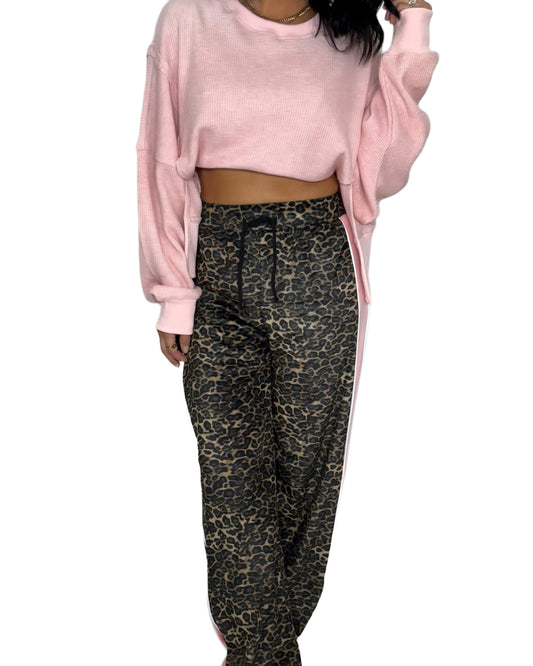 Person wearing a pink long-sleeve top and leopard print pants on a white background