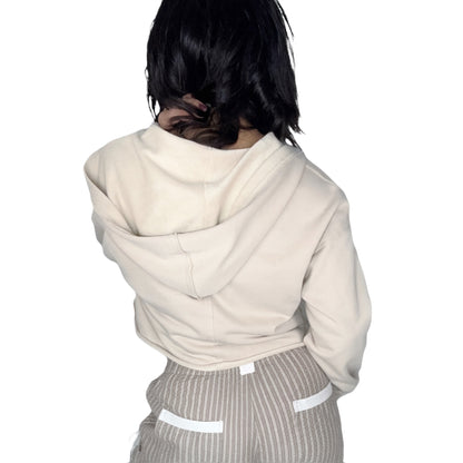 Back profile of a woman wearing a tan hooded top and striped pants on a white background