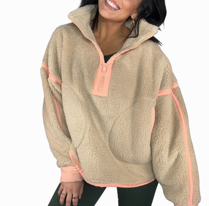 Woman wearing a taupe fleece pullover with peach accents on a white background