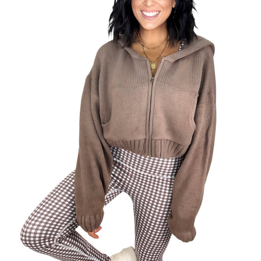 Woman wearing a brown knit zip-up jacket and brown gingham active bottoms on a white background
