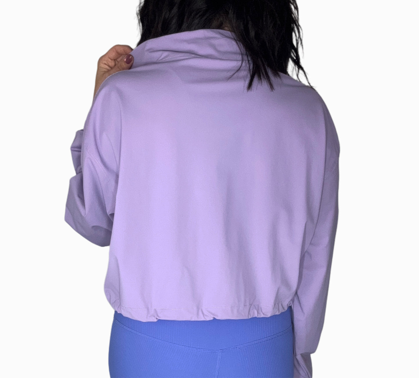 Back profile of a woman wearing a purple half-zip jacket and blue leggings on a white background