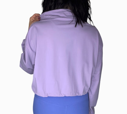 Back profile of a woman wearing a purple half-zip jacket and blue leggings on a white background