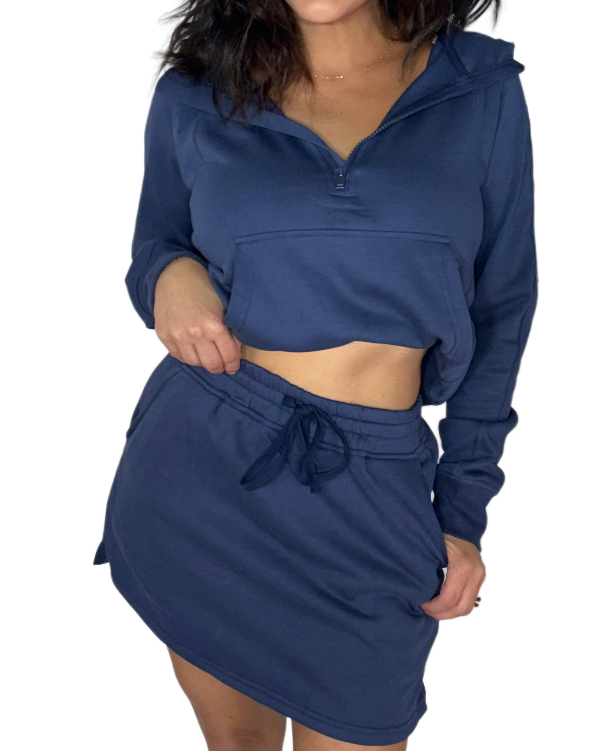 Close profile of a woman wearing a matching navy blue loungewear set , half-zip hoodie and a drawstring mini skort, shown against a plain white background