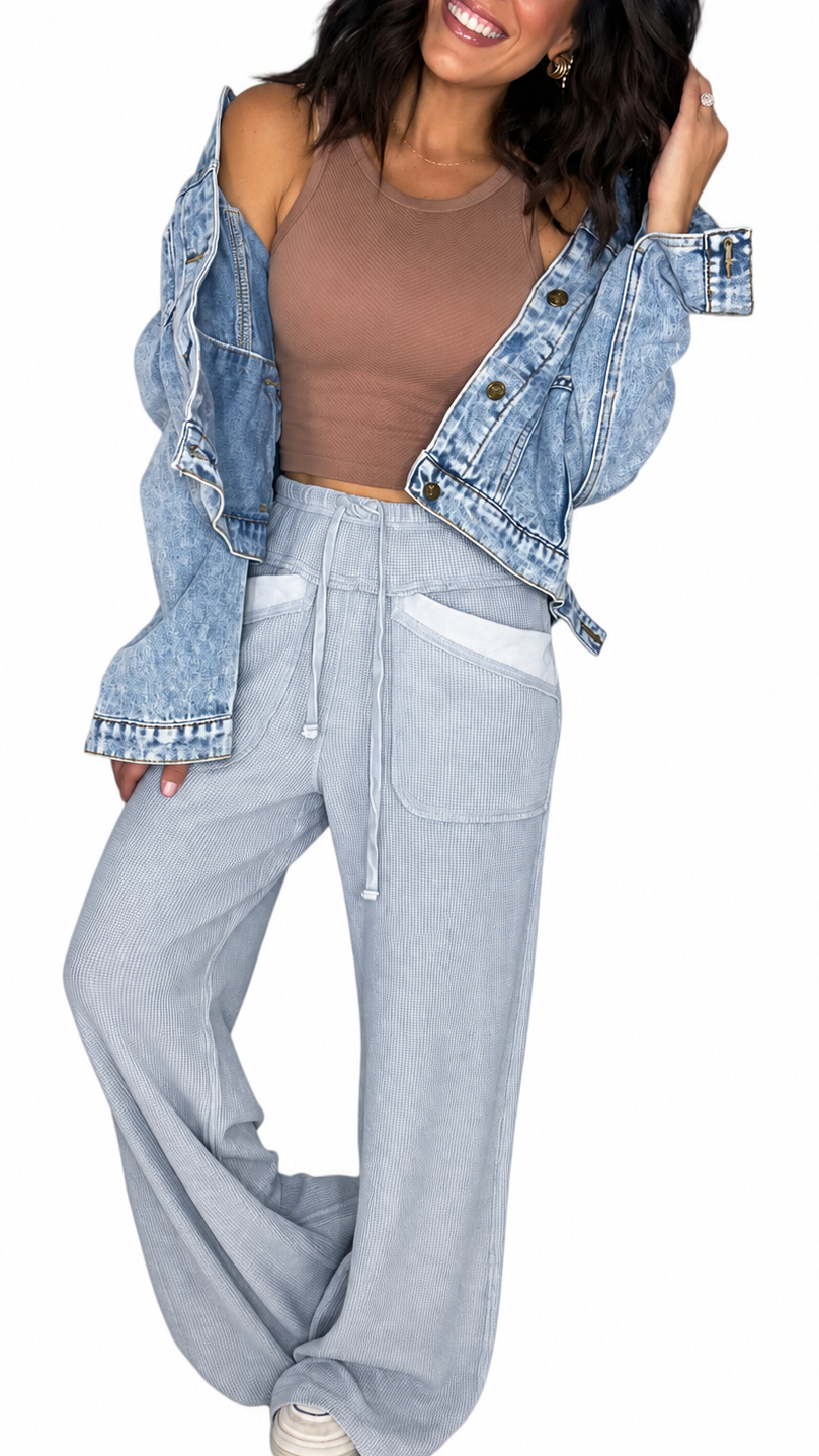 Woman wearing waffle light blue casual pants with a drawl string and front pockets with a brown tank and jean jacket on a white background