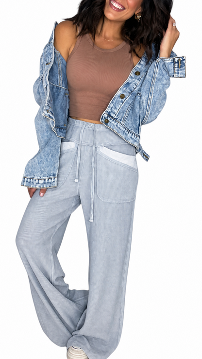 Woman wearing waffle light blue casual pants with a drawl string and front pockets with a brown tank and jean jacket on a white background