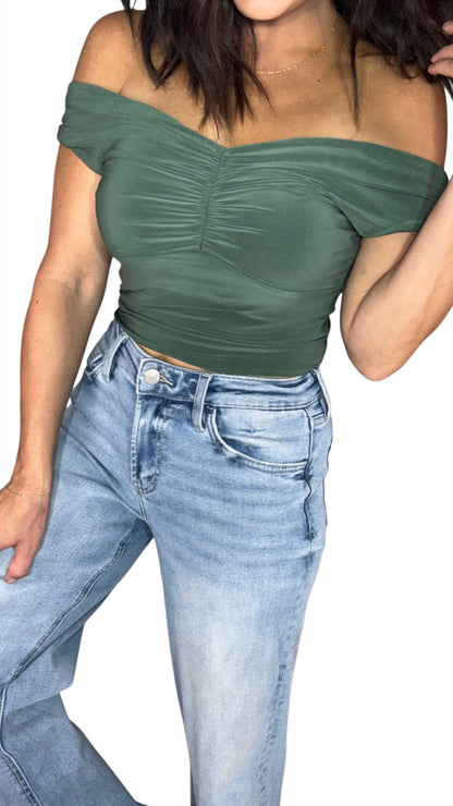 Close up of a woman wearing a olive green off the shoulder crop top with medium washed jeans, on a white background
