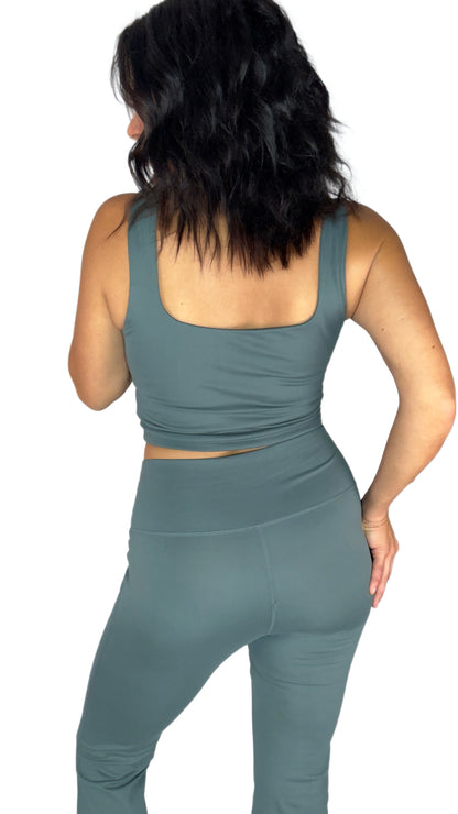 Back profile of a woman wearing a matching active flared pant set and tank top in Eucalyptus on a white background 