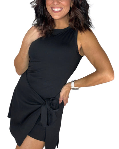 Side profile of a woman modeling a sleeveless black mini active romper  with a side-tie detail, set against a plain white background.