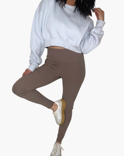 Woman wearing ribbed deep taupe leggings, a cropped light blue sweatshirt, on a white background.