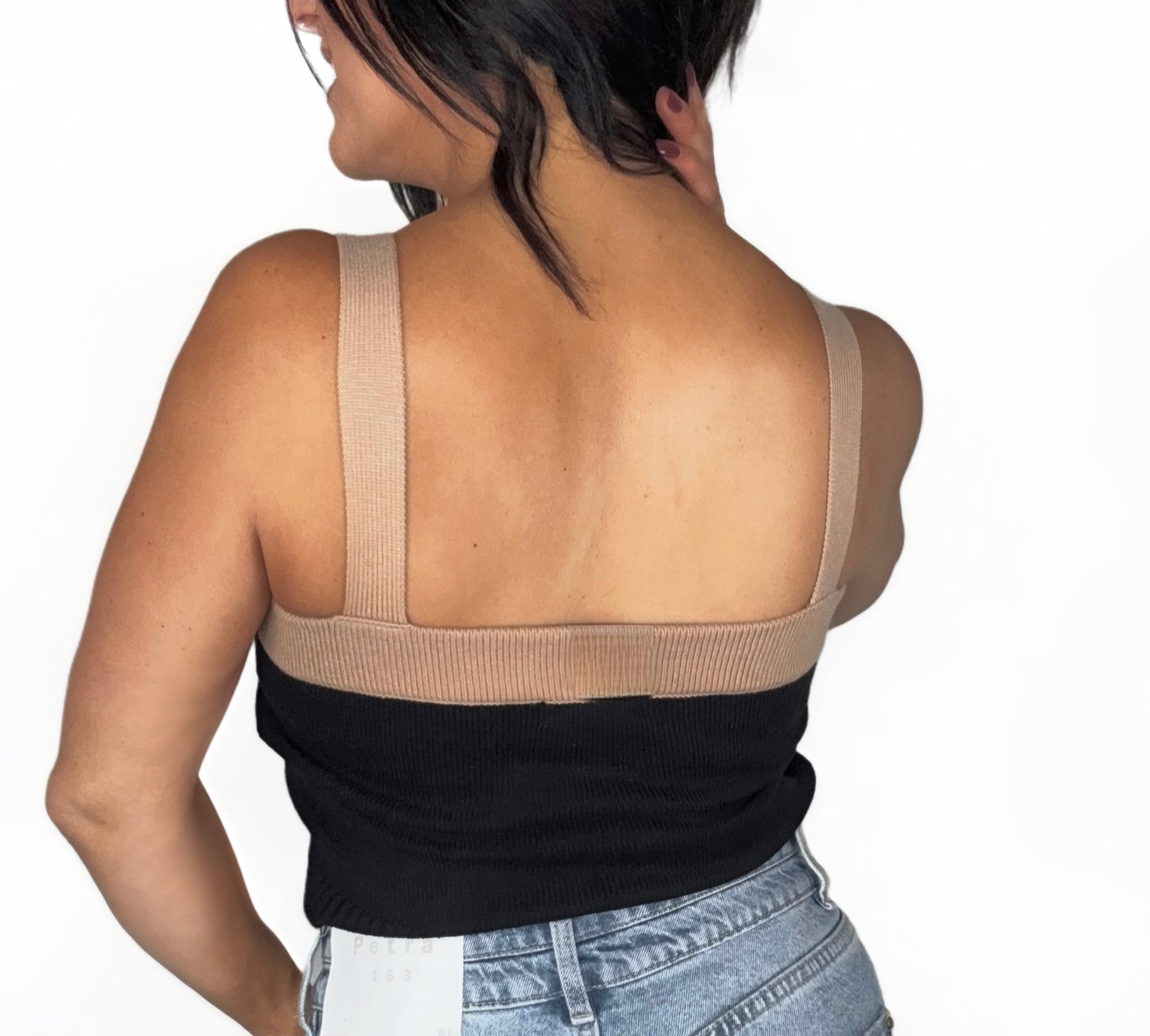 Back profile of a woman wearing a black and beige button-up crop top with high-waisted jeans on a white background