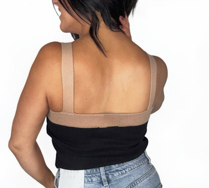 Back profile of a woman wearing a black and beige button-up crop top with high-waisted jeans on a white background