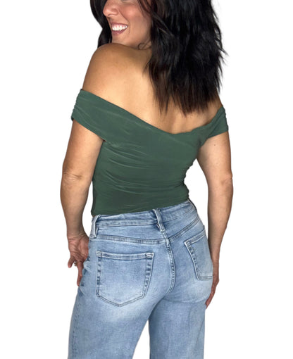 Back profile of a woman wearing a olive green off the shoulder crop top with medium washed jeans, on a white background