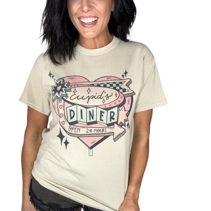 Woman wearing a sand color t-shirt with 'Cupid's Diner' graphic design on a plain background