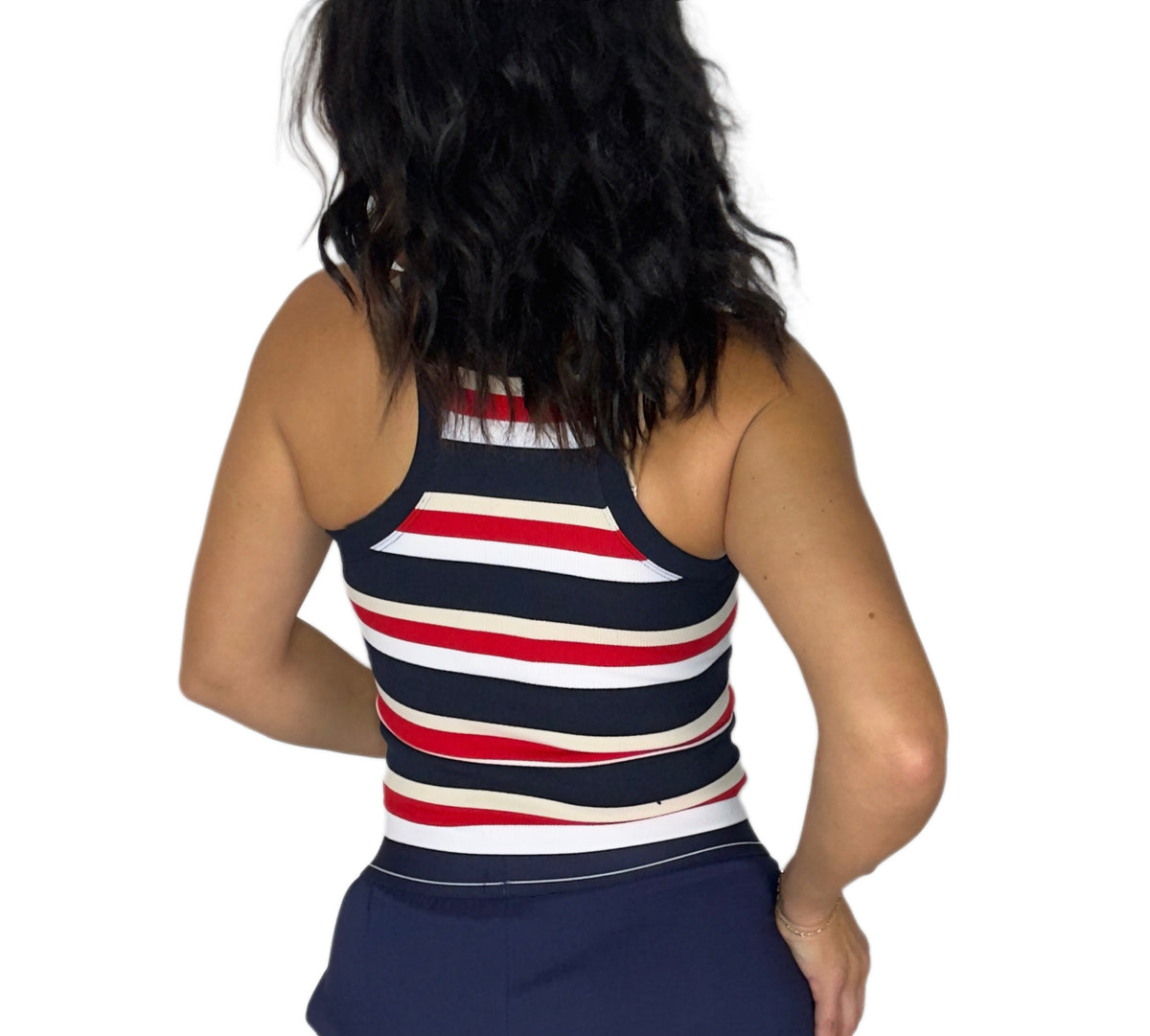 Back profile of a woman wearing a striped red, blue, white and tank tank with navy bottoms on a white background