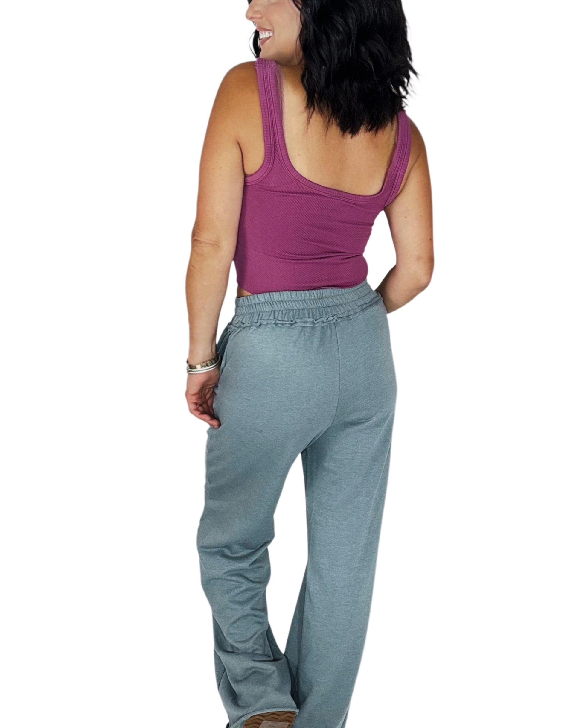 Back profile of a woman wearing a ribbed mauve tank top with blue grey sweat pants on a white background