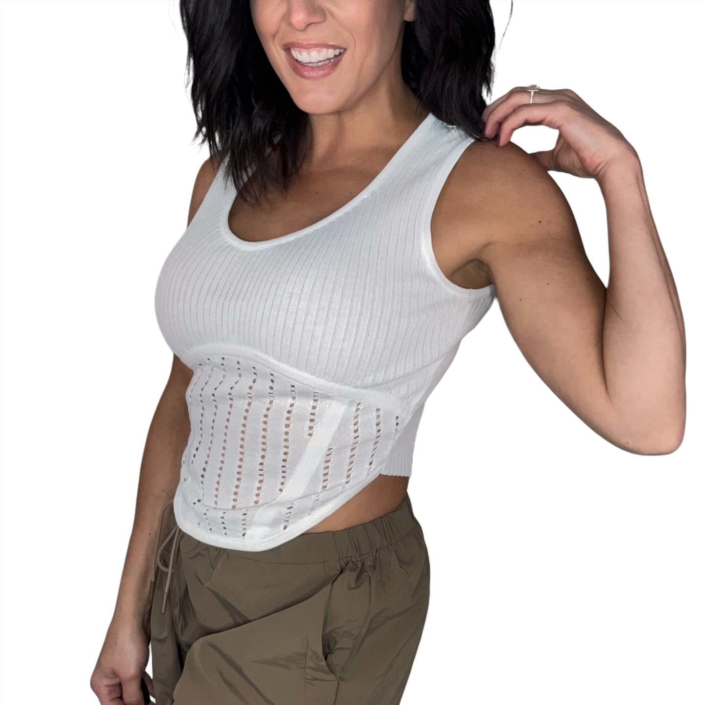 Side profile of a woman wearing a white knit tank top with green pants and a white background 