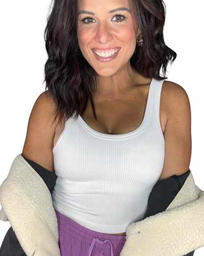 Woman wearing a ribbed active tank top with a sherpa jacket hanging off her shoulders, lilac bottoms, on a white background 