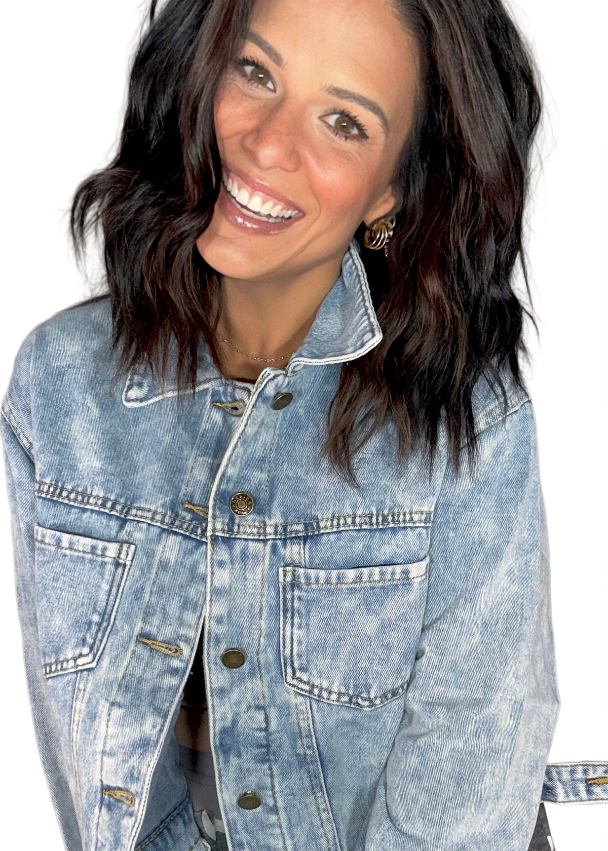 Woman smiling while wearing a light washed denim boxy jean jackets with camo pants, on a white background 