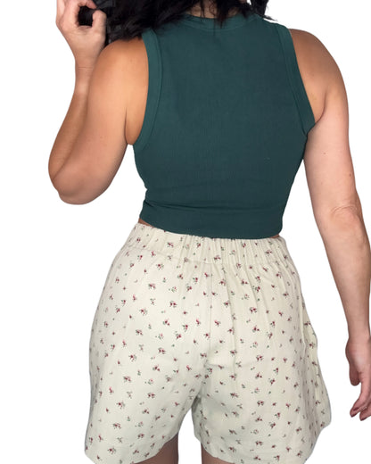 Back profile of a woman wearing floral shorts and a green top on a white background