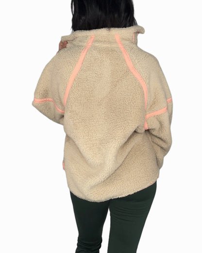 Back profile of a woman wearing a taupe fleece pull over with peach accents on a white background