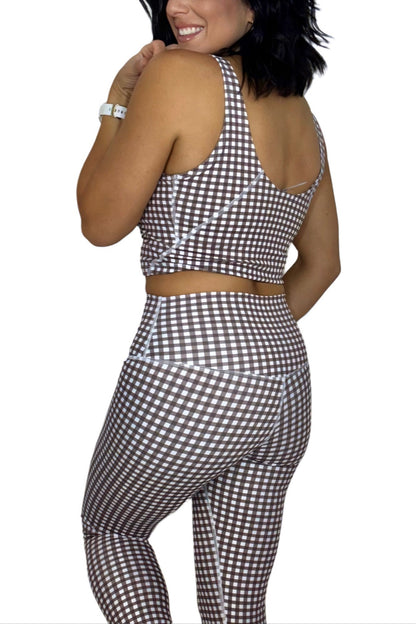 Woman turned around wearing a brown and white gingham athletic set on a white background